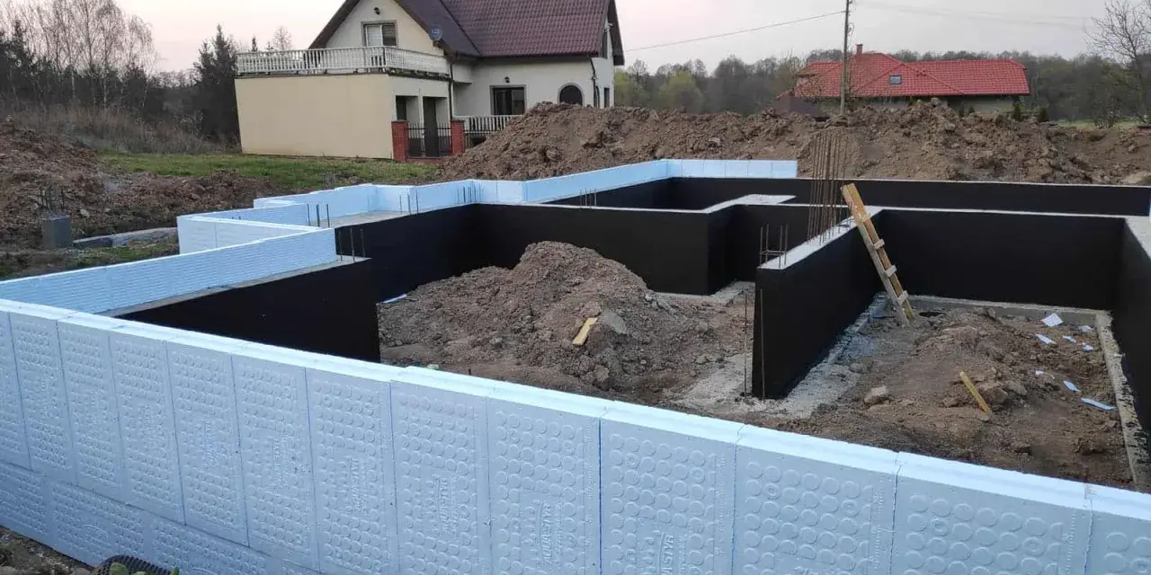 Budowa domu: jak ocieplić fundament styropianem. Widoczne elementy izolacji fundamentów, zbrojenia i ziemia.