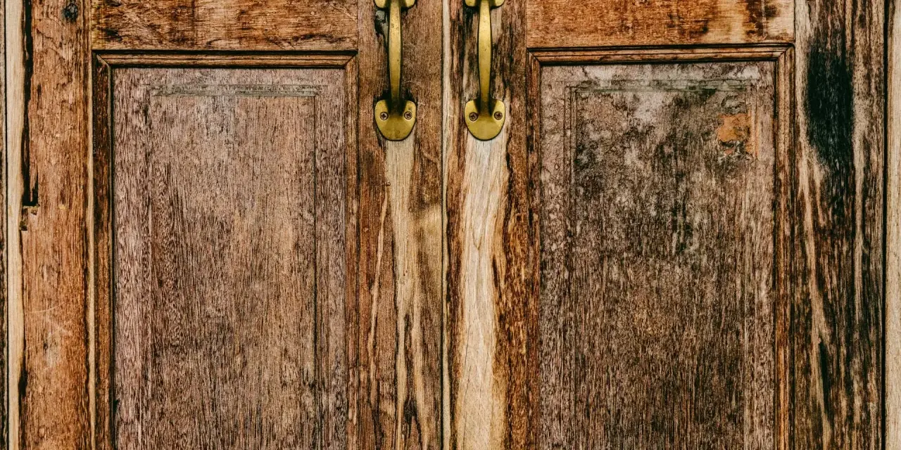 Zbliżenie na stare, drewniane drzwi z dwoma mosiężnymi uchwytami.