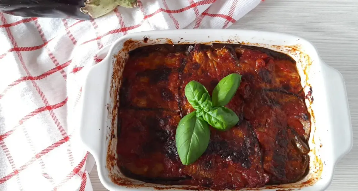 Parmigiana di melanzane non fritte, appena sfornata, guarnita con basilico fresco. La ricetta perfetta per un piatto leggero e gustoso.