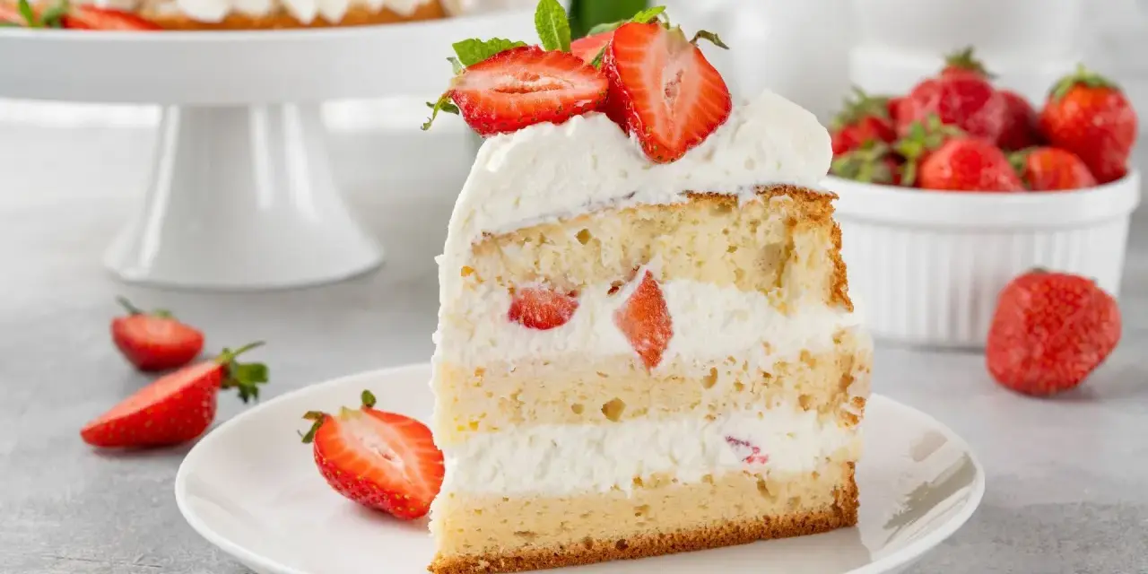 Puszysty biszkopt przełożony kremową masą z mascarpone i kawałkami truskawek, udekorowany świeżymi owocami.