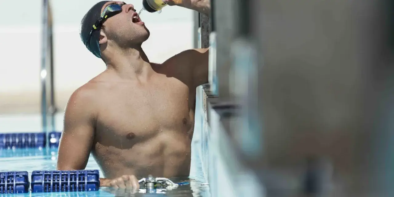 Un nageur en bonnet et lunettes boit dans une bouteille, prêt à apprendre comment nager.