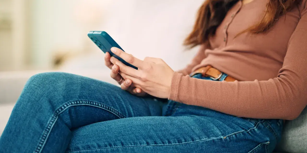 Kobieta w dżinsach i bluzce z długim rękawem trzyma telefon. To może być obraz skutków zbyt długiego korzystania z telefonu.