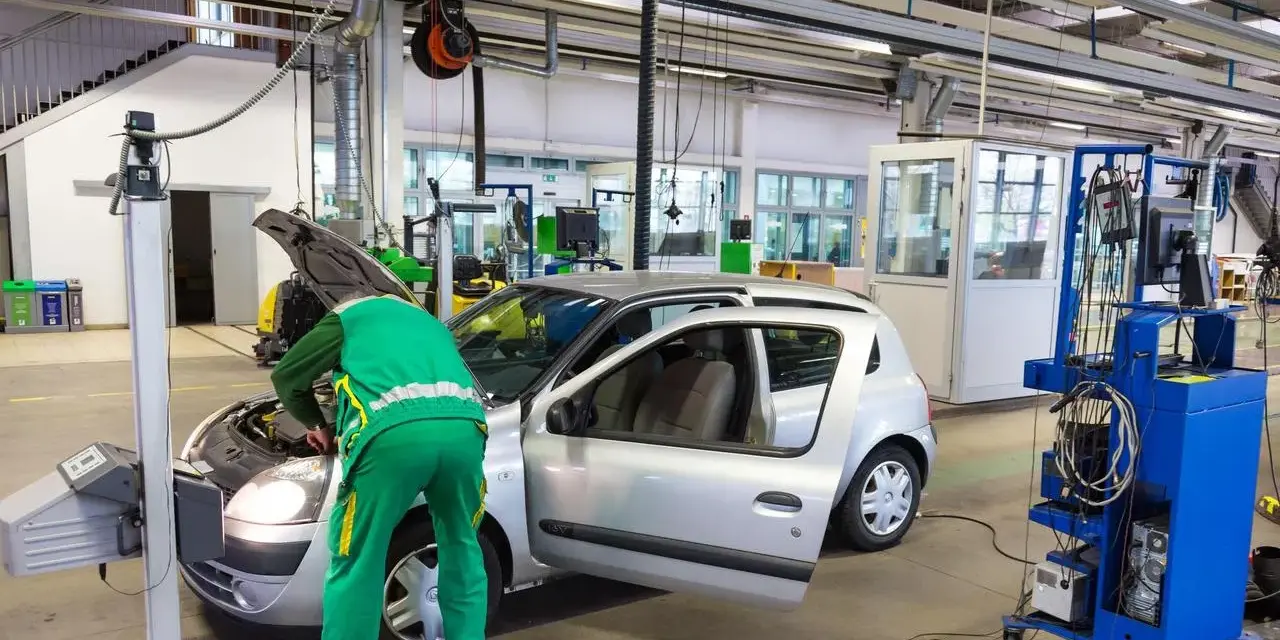 Un meccanico in tuta verde controlla un'auto argentata in un'officina, forse per un controllo secondo l'articolo 80 del codice della strada.