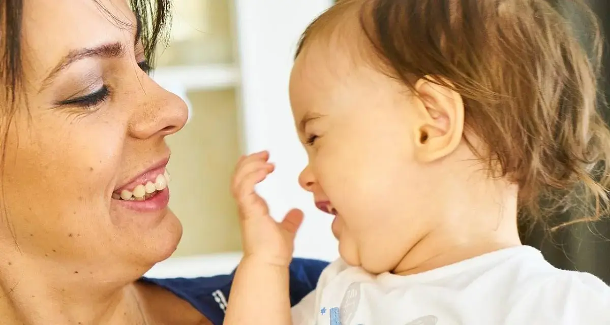 Uśmiechnięta mama patrzy na swoje dziecko, które bawi się i śmieje, wyciągając rączkę.