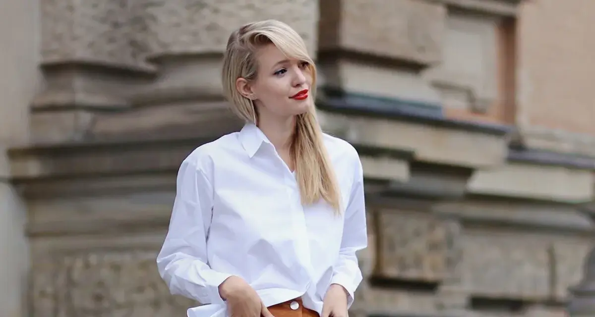 Mujer con falda de gamuza y camisa blanca, posando con las manos en los bolsillos.