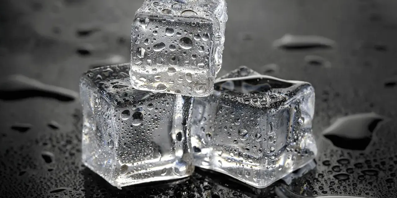 Drei eiswürfel mit Wassertropfen auf schwarzem Hintergrund. Die Frage, wie lange braucht Eis zum Gefrieren, wird hier visuell beantwortet.