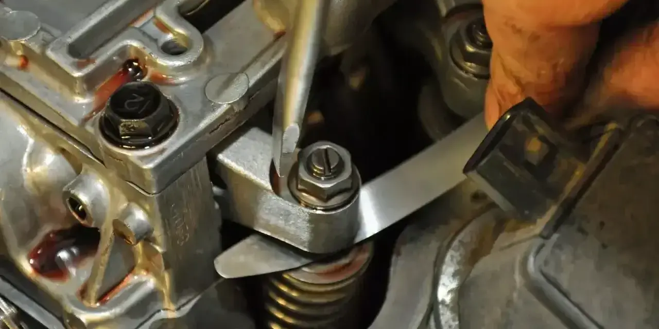 Mechanik reguluje zawory w silniku, używając śrubokręta i szczelinomierza.