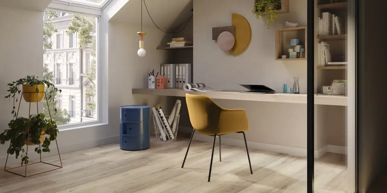 Luminoso studio mansardato con scrivania, sedia gialla e un elegante **pavimento polvere di pietra** che riflette la luce naturale.