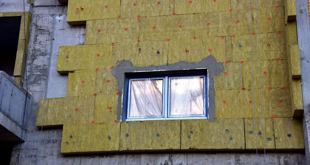 Pannelli di lana di roccia per cappotto termico spessore, fissati con tasselli rossi su un edificio in costruzione.