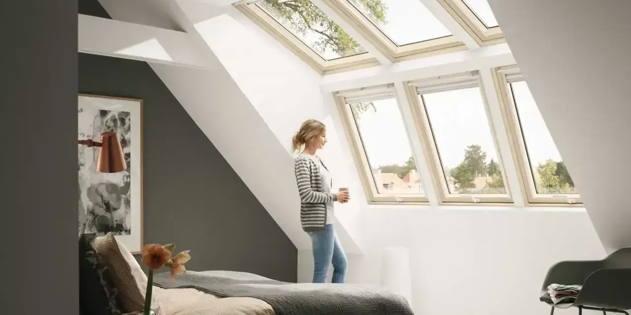 Kobieta w sypialni pod jasną, nowoczesną lukarną dachową, podziwia widok.