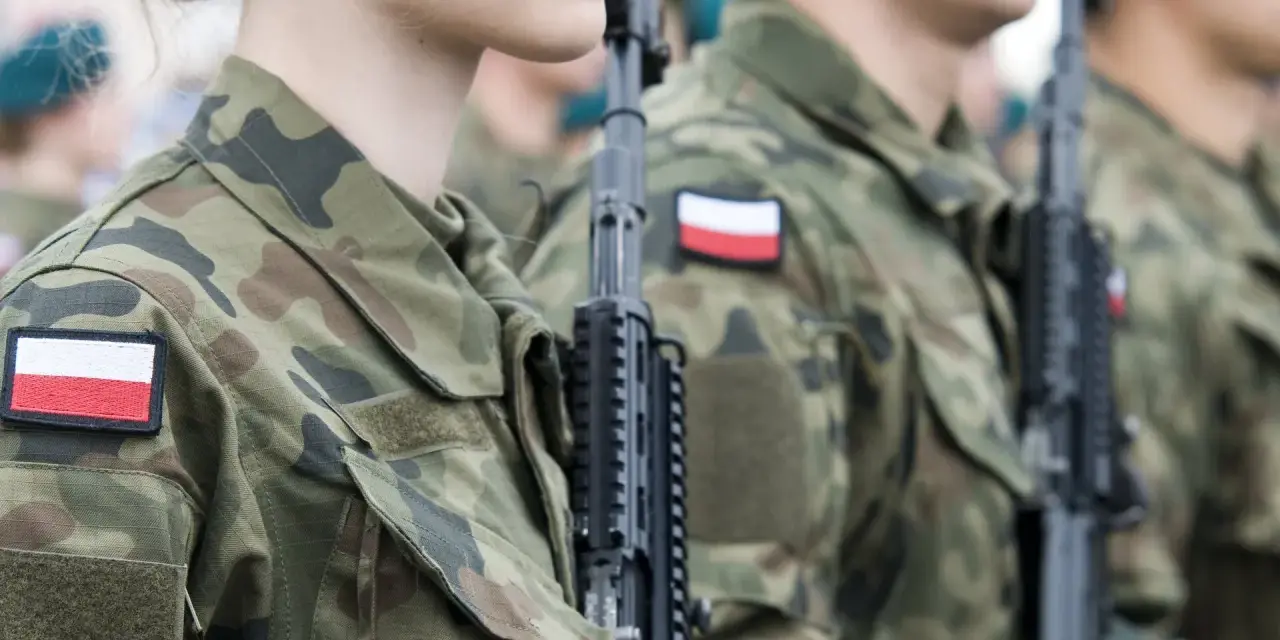 Żołnierze w mundurach z polskimi flagami, gotowi do marszu. Słychać przyśpiewki wojskowe.