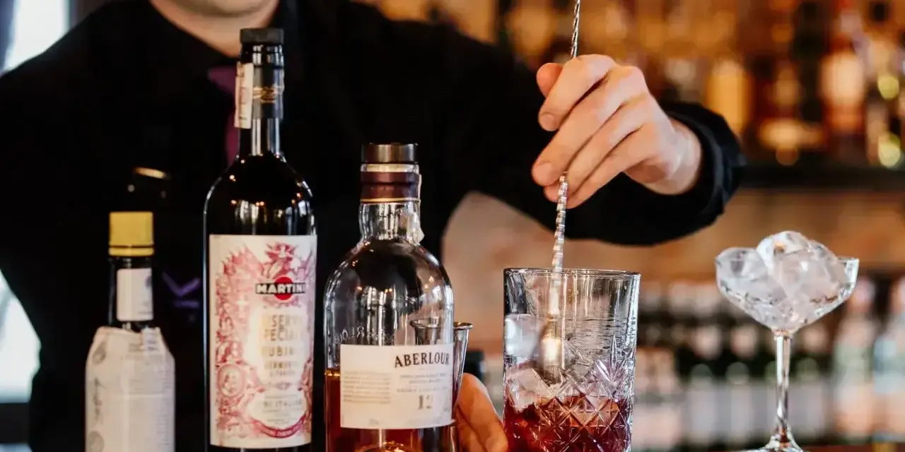Barman miesza składniki, przygotowując najlepszy drink z whisky. Na blacie butelki Aberlour, Martini i inne.
