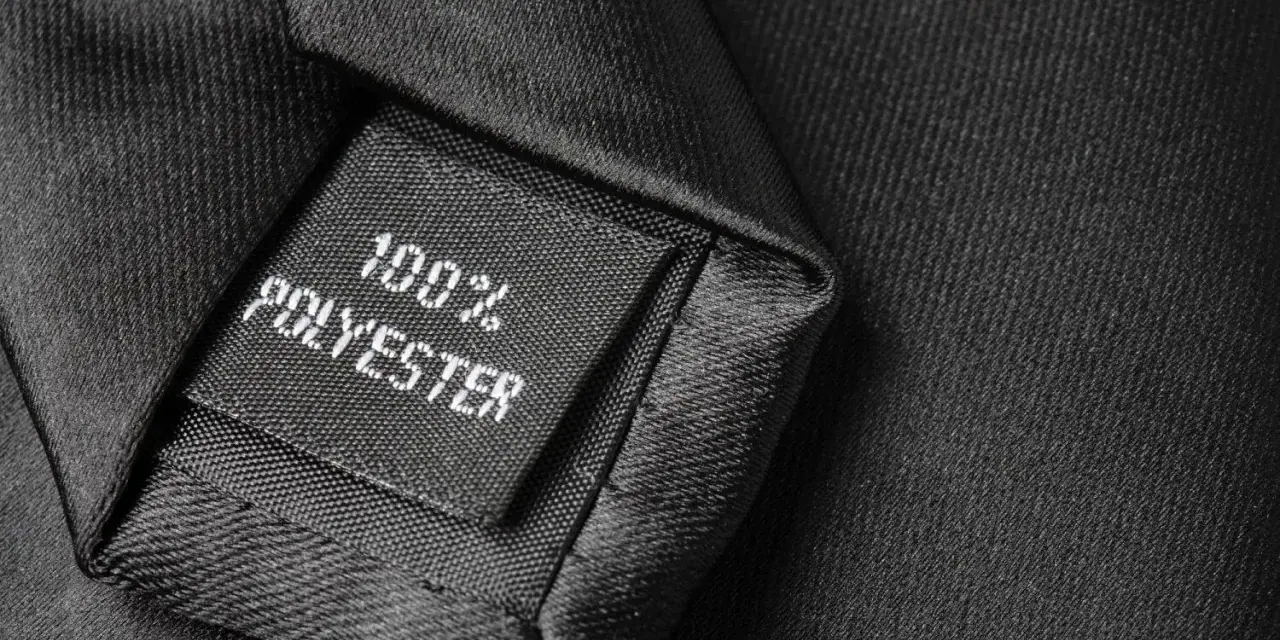 Czarna metka z napisem "100% POLYESTER" na tle eleganckiego materiału. Czy poliester to dobry materiał?