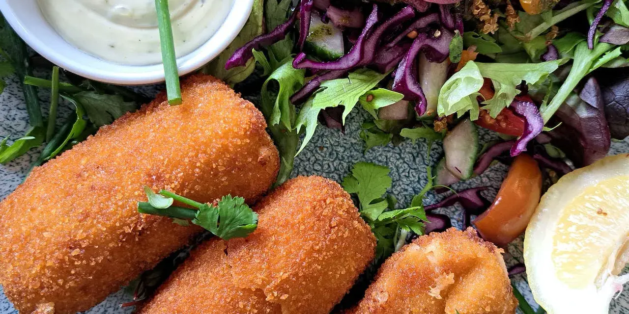 Croquetas doradas y crujientes con ensalada fresca, salsa y limón.