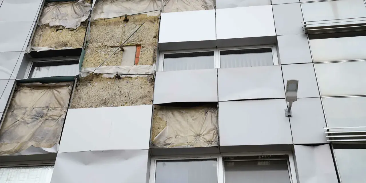 Facciata di un edificio con pannelli rimossi, mostrando l'isolamento. Si valuta la conducibilità termica dei materiali per l'efficienza energetica.
