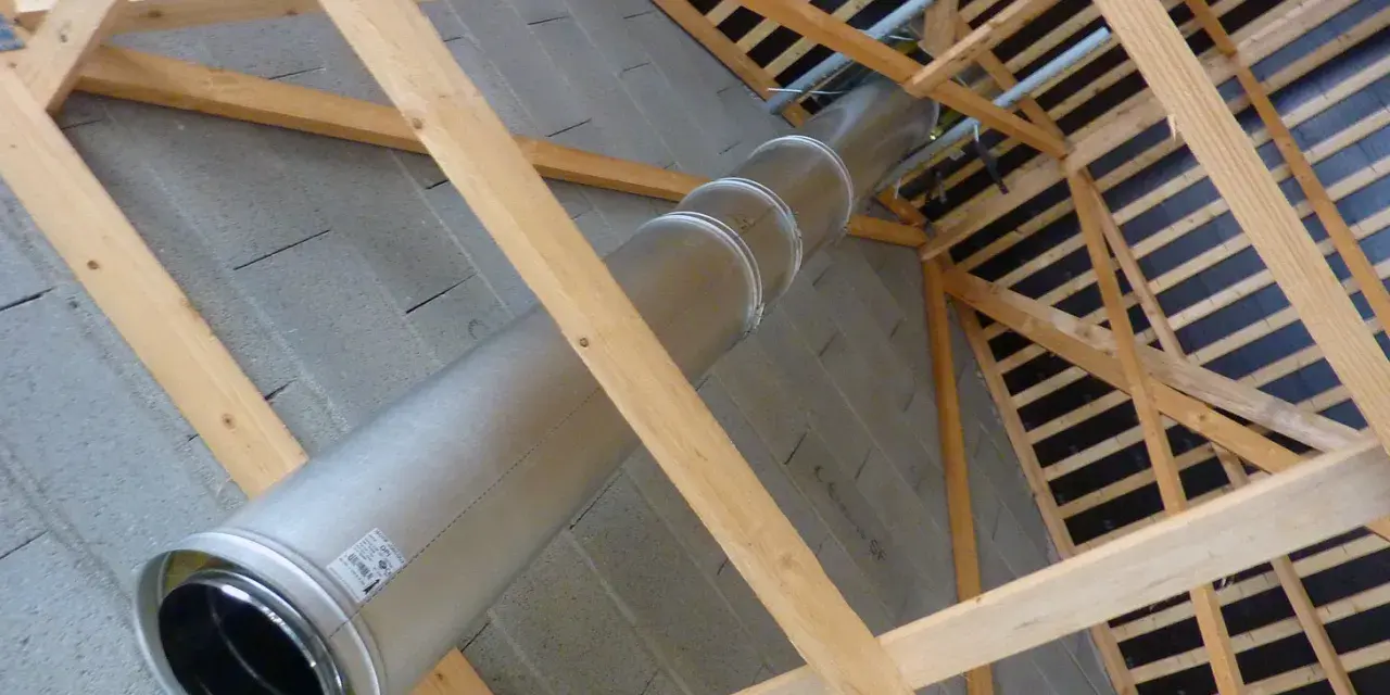 Installation d'un tubage cheminée en métal dans une charpente en bois. Le conduit traverse un mur en parpaings.