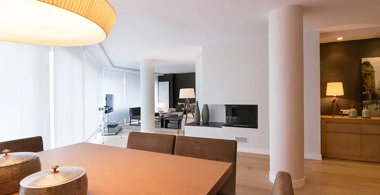 Comedor y salón modernos tras reforma piso pequeño. Mesa de madera, chimenea y mobiliario elegante.