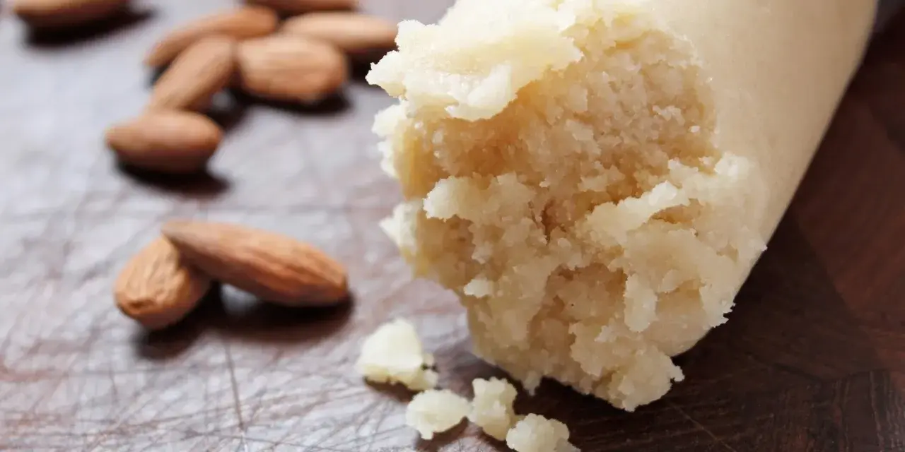 Frische Mandeln liegen neben einer Rolle Marzipan Rohmasse, bereit zum Verarbeiten.