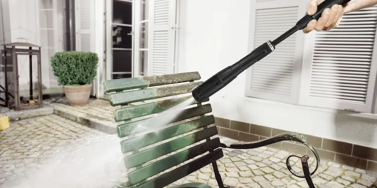 En Kärcher K5 rengör en smutsig grön parkbänk utomhus.