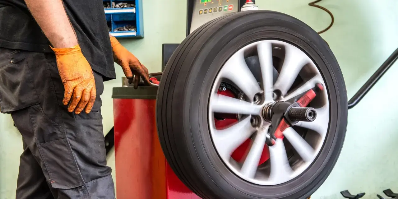 Meccanico con guanti arancioni controlla la vibrazione auto semiasse su una macchina bilanciatrice.