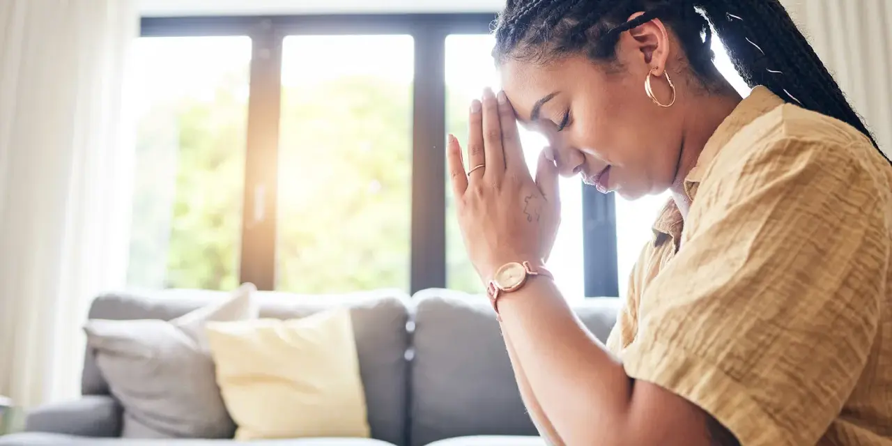 A woman with braided hair and hoop earrings prays with her hands clasped, finding peace during her christian prayer times.