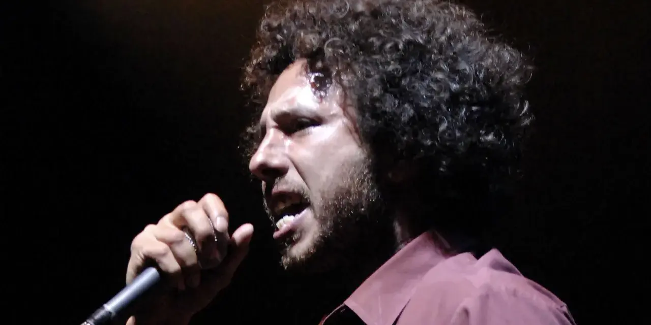 Zack de la Rocha heute, mit seinem charakteristischen lockigen Haar und einem Mikrofon in der Hand, singt leidenschaftlich auf der Bühne.