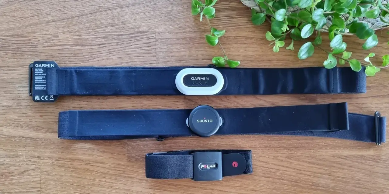 Tre pulsbands från Garmin, Suunto och Polar ligger på ett trägolv. Jämför garmin pulsband skillnad med de andra.