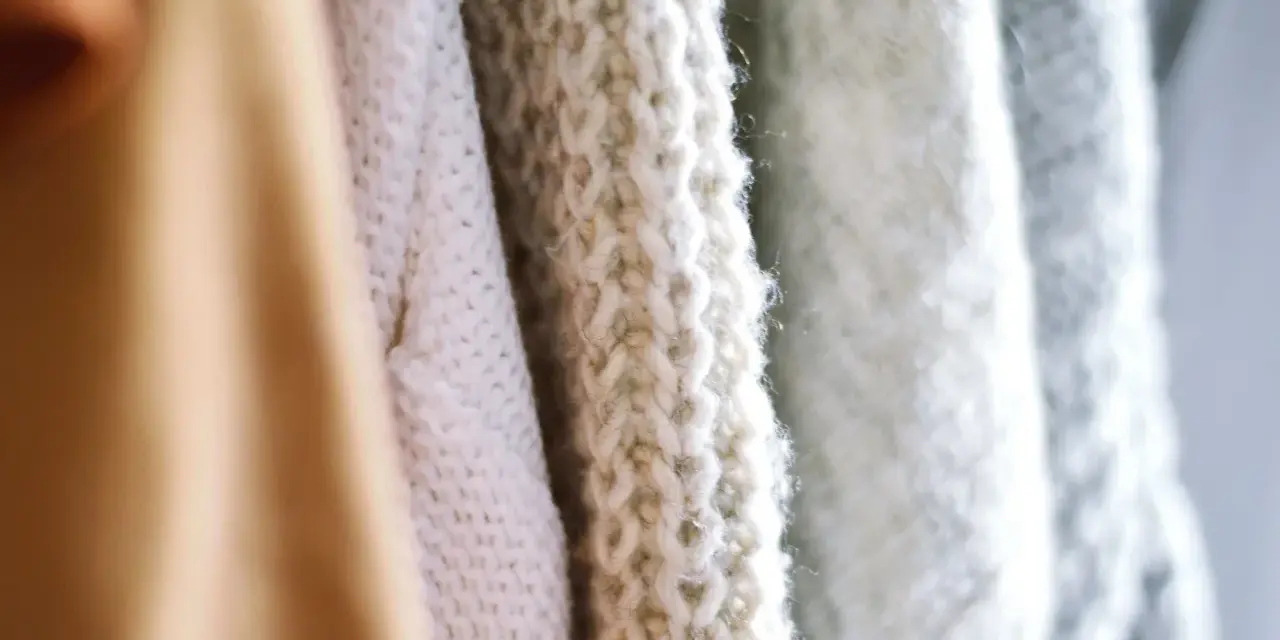 Nahaufnahme von Strickwaren in verschiedenen Pastelltönen. Die feine Struktur zeigt, dass Merinowolle fusselt, was den weichen Charakter unterstreicht.