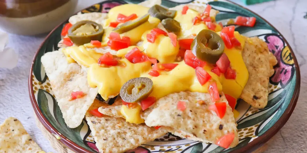 Nachos con queso derretido, jalapeños y tomate picado en un plato decorado.