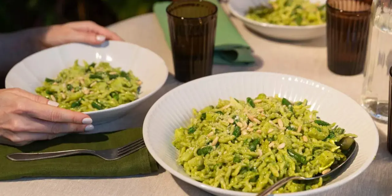Due piatti di trofie al pesto, condite con fagiolini e pinoli, pronte per essere gustate.