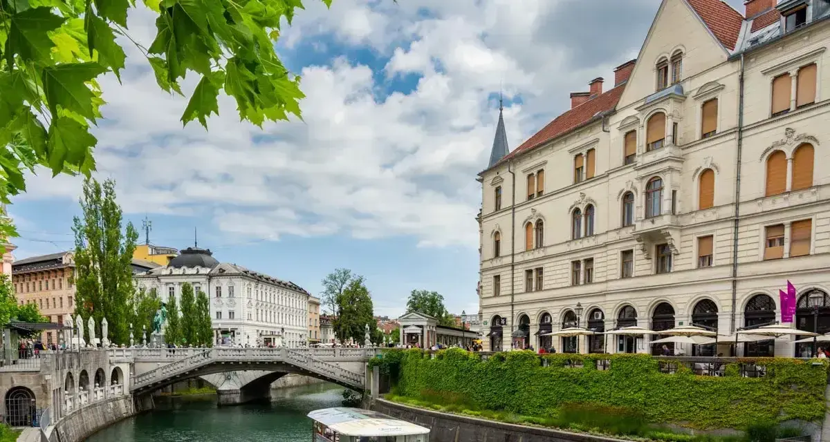 Lublana co zobaczyć: malowniczy widok na rzekę Ljubljanicę, most i zabytkowe budynki. Rejs statkiem to świetny sposób na zwiedzanie.