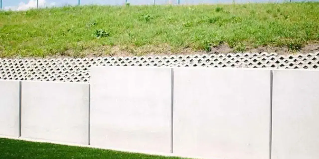 Betonowy mur oporowy z ażurową warstwą i zieloną skarpą.