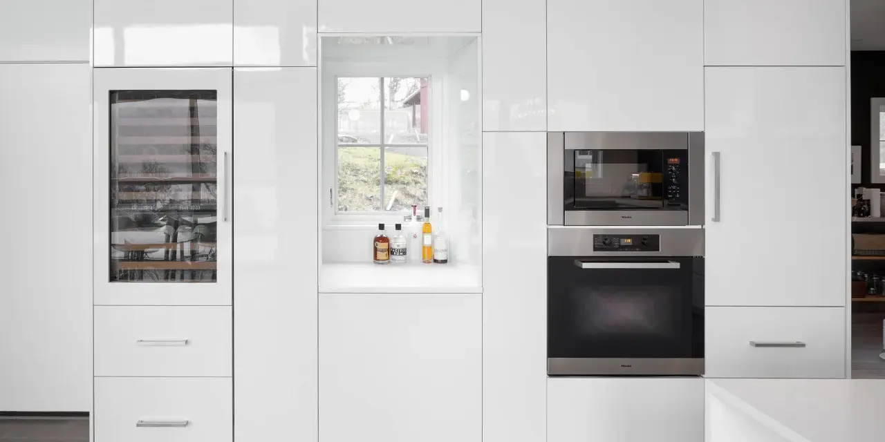 Cucina moderna bianca con elettrodomestici integrati e una porta finestra che offre una vista sul verde.