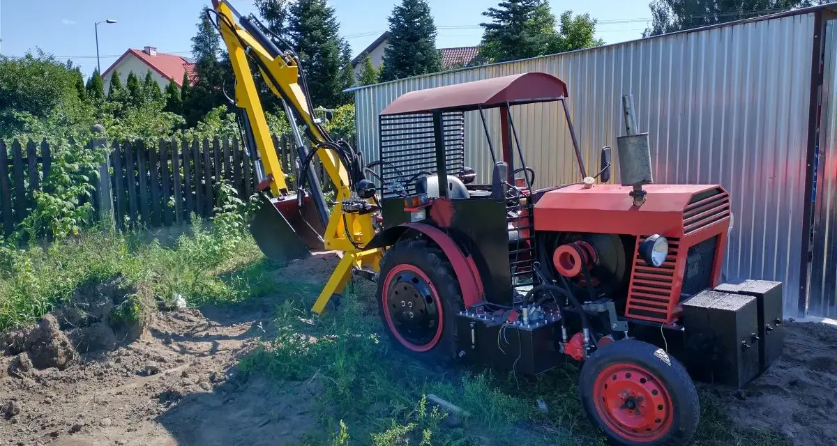 Czerwony traktor C-330 z zamontowaną żółtą koparką, gotowy do pracy w ogrodzie.