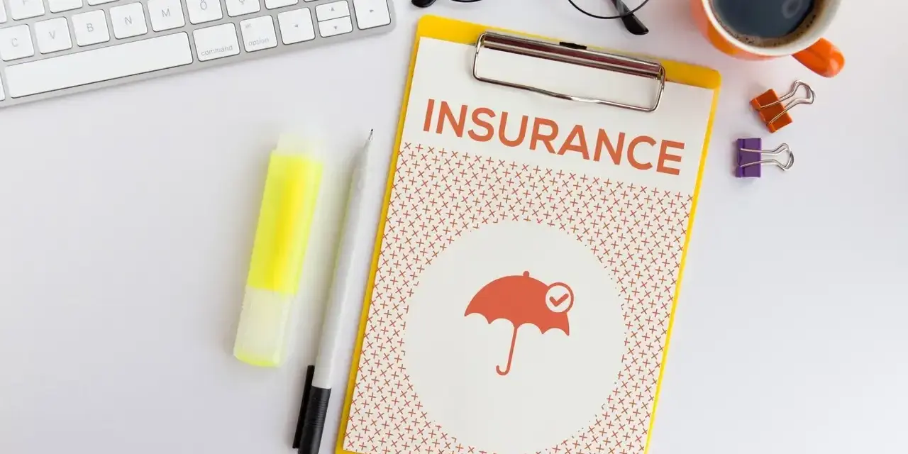 Dokument "Insurance" z parasolką, klawiatura, okulary, kawa. Planowanie ubezpieczenia zdrowotnego bez pracy.