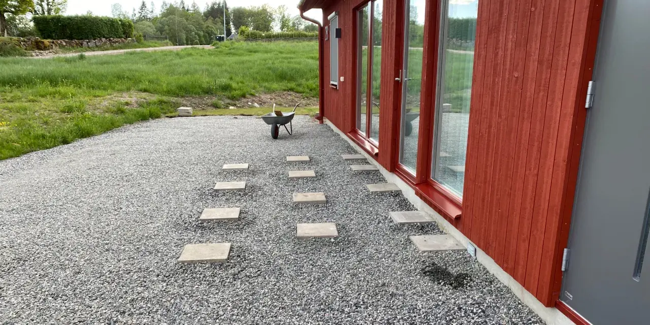 Stigande steg av altan plintar eller plattor leder genom grusgången fram till ett rött hus med stora fönster.