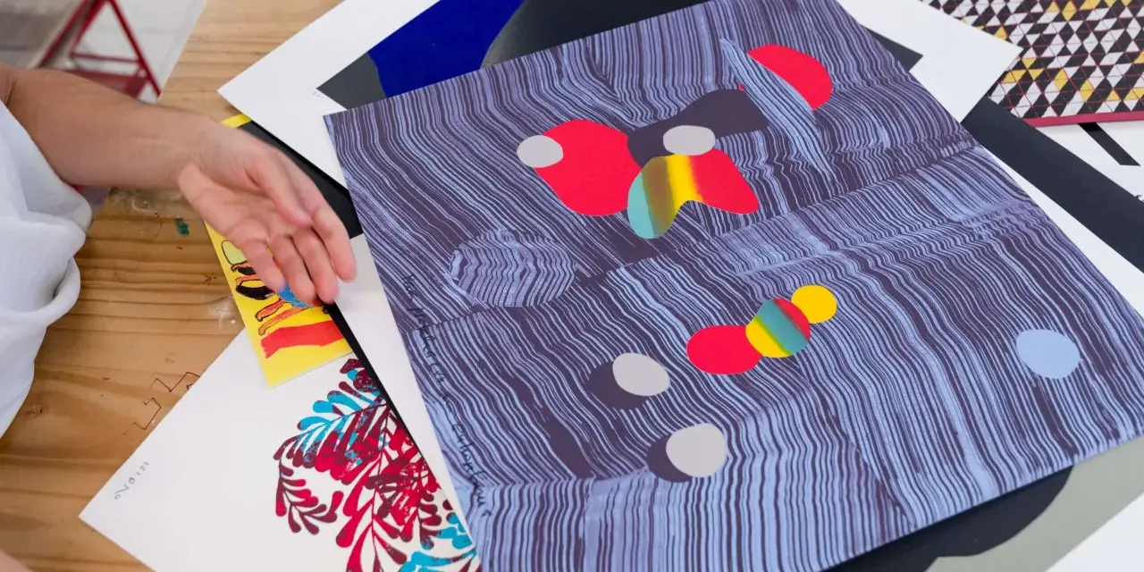 Manos revisando impresiones de arte abstracto, con vibrantes colores y patrones. El material serigrafia resalta en cada detalle.