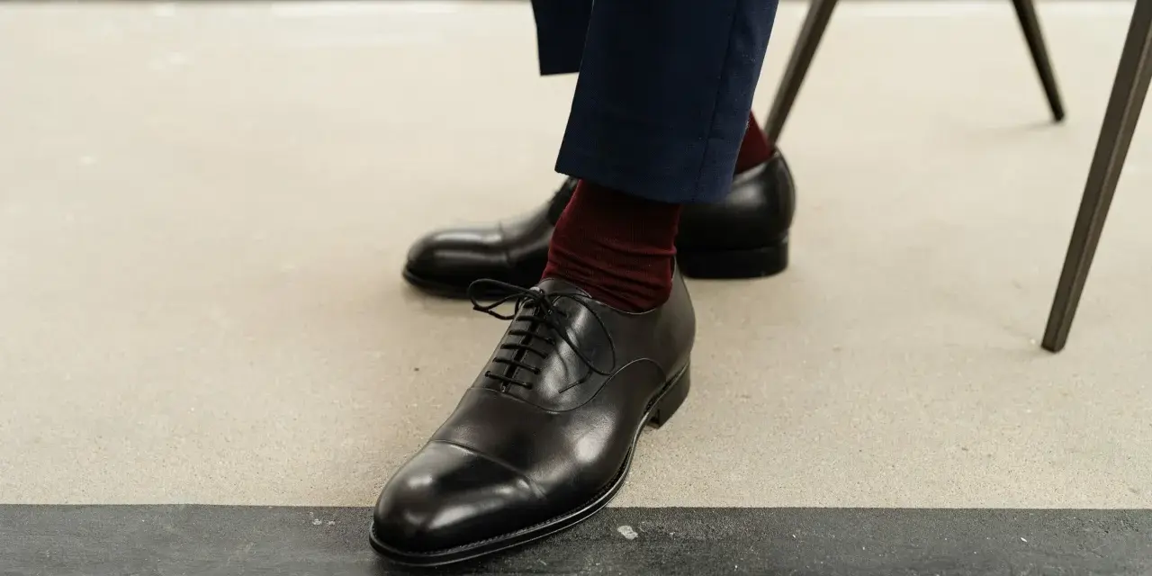 Eleganckie czarne buty męskie, rozmiar buta 50, z bordowymi skarpetkami i granatowymi spodniami.