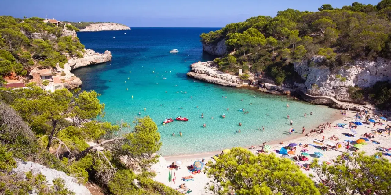 Rajska zatoka z turkusową wodą i piaszczystą plażą, pełna ludzi. To jedna z najpiękniejszych plaż w Hiszpanii.