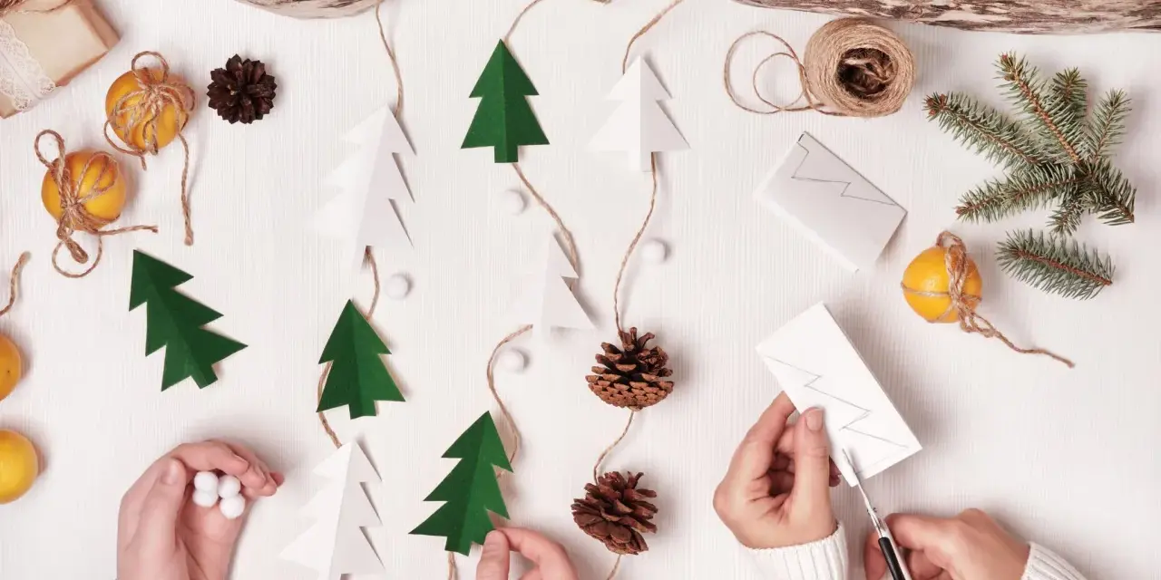 Kinder basteln Weihnachtsgeschenke: Papierbäume, Zapfen und Orangen werden zu einer festlichen Girlande.