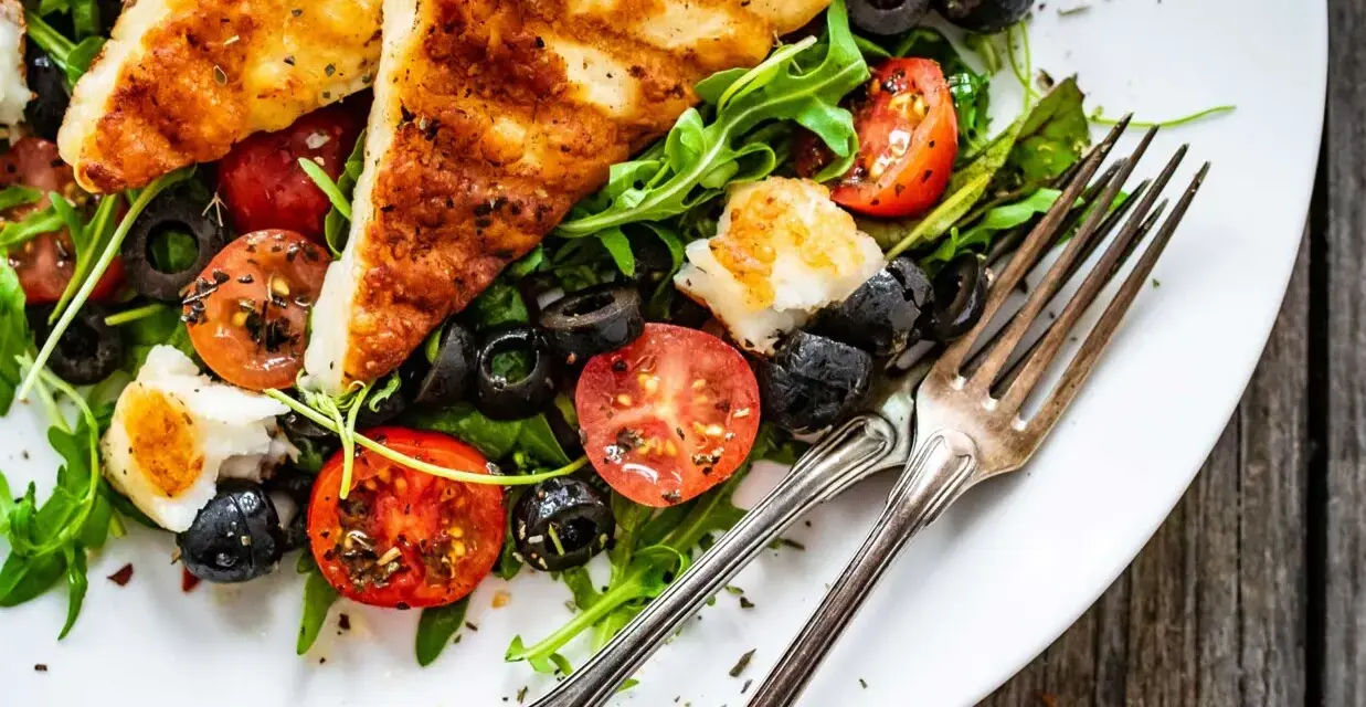 Pyszna sałatka z grillowanym halloumi, pomidorkami koktajlowymi i czarnymi oliwkami na talerzu.