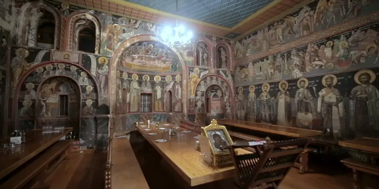 Inside Mount Athos, a refectory is adorned with ancient frescoes depicting religious scenes and figures.