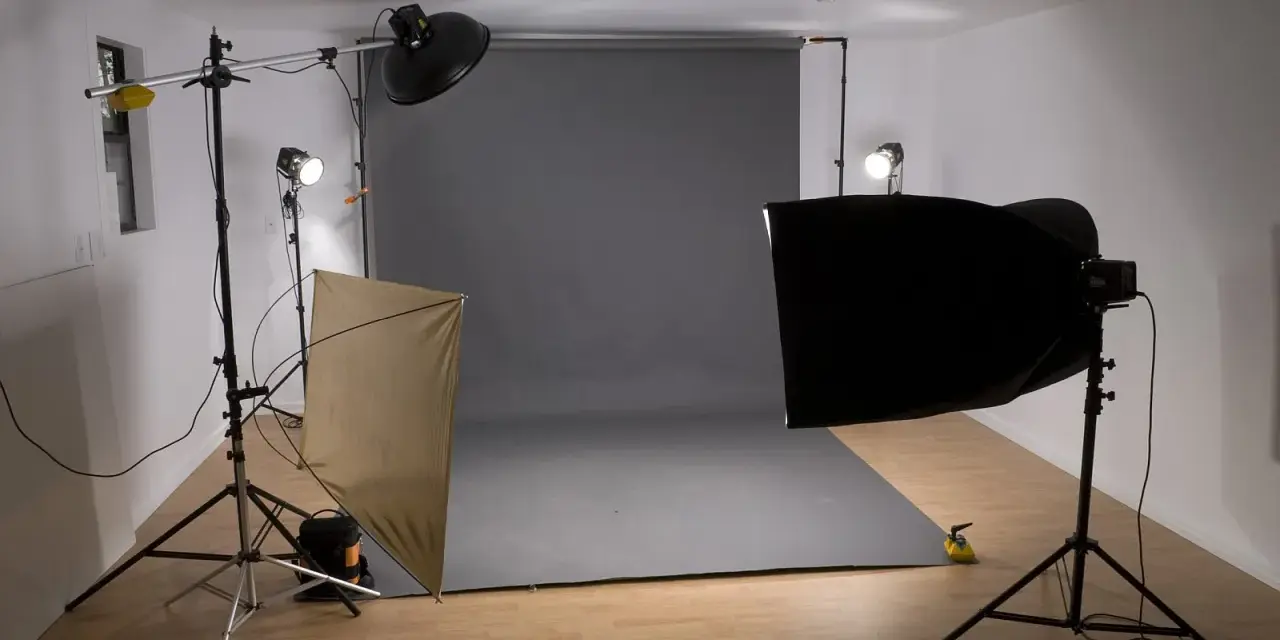 Studio fotograficzne z szarym tłem, lampami i dyfuzorem. Światło kontrowe tworzy dramatyczne cienie.