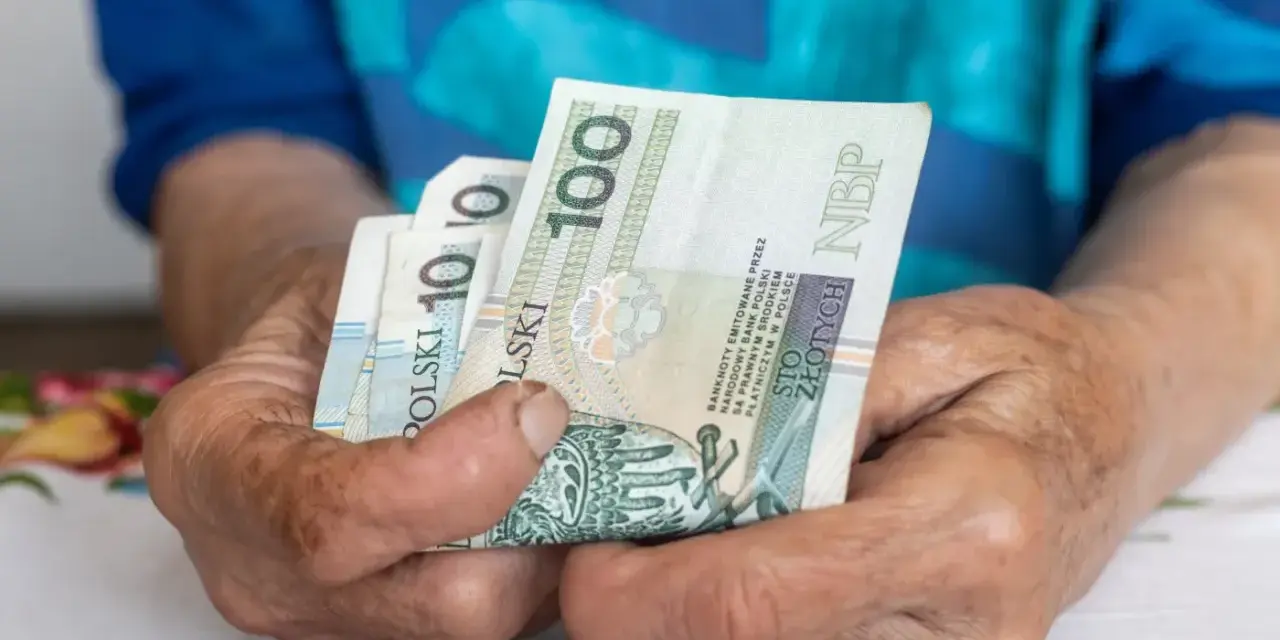 Dłonie starszej osoby trzymają banknoty 100 zł. Czy to wystarczy na godne życie, gdy średnia emerytura w Polsce jest taka, jaka jest?