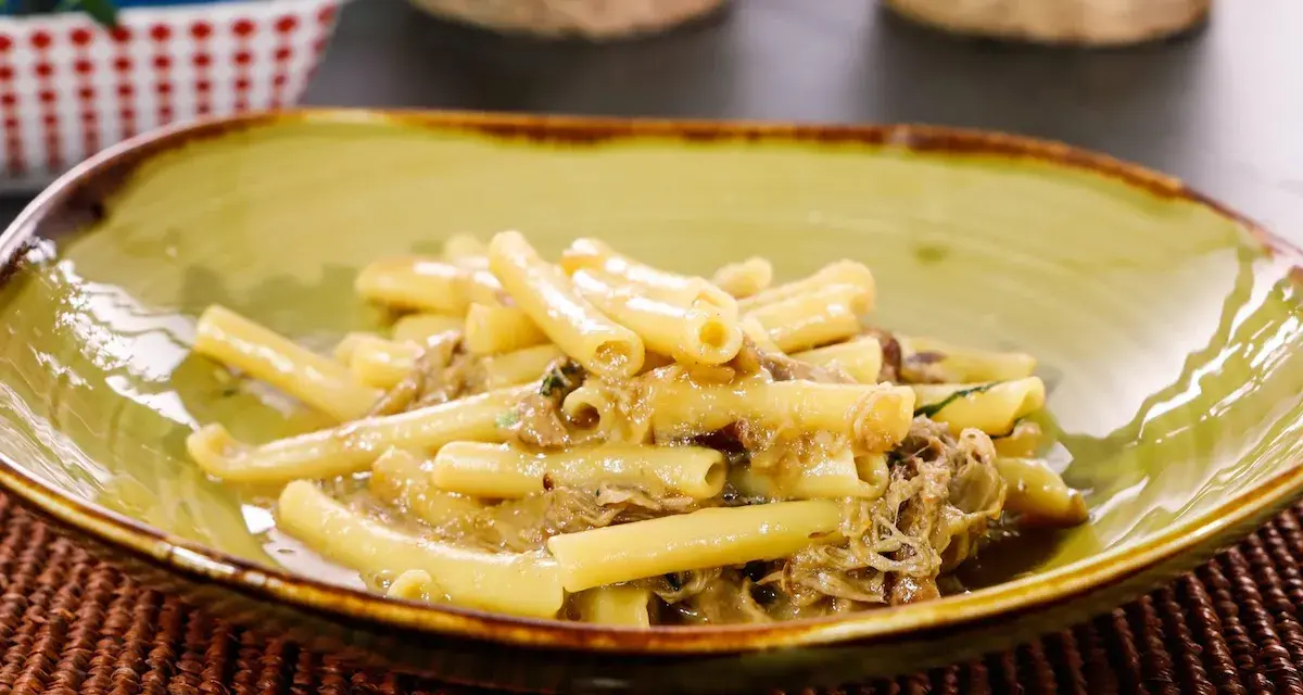 Piatto di ziti alla genovese, pasta condita con un ricco ragù di carne, servita in una ciotola verde.