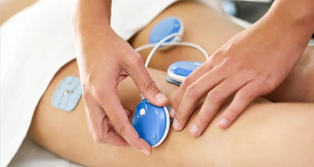 Fizykoterapia co to? Terapeuta umieszcza elektrody na nodze pacjenta, co jest częścią zabiegu.