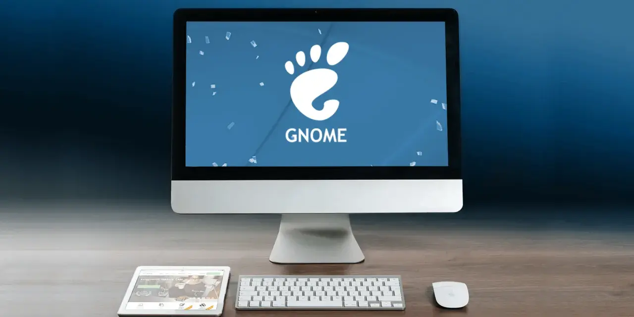 Komputer z logo GNOME, tablet i klawiatura na drewnianym biurku.