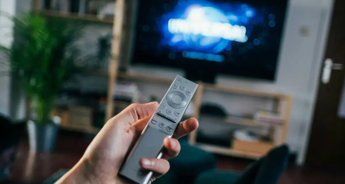 Dłoń trzymająca srebrny pilot do telewizora, na ekranie logo Universal.