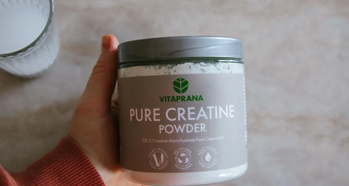En hand håller en burk med Vitaprana Pure Creatine Powder. Kan vara ett komplement för den som vill ha **kreatin viktnedgång**.