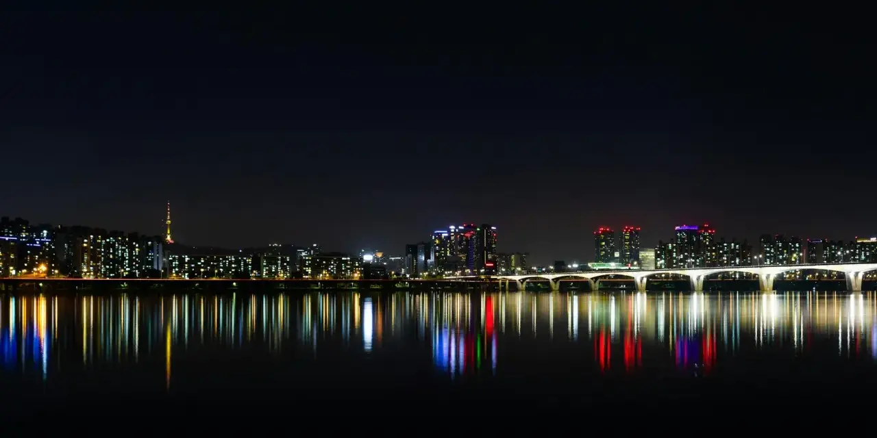 Nocny widok na Seul z rzeką Han, mostem i wieżą Namsan. Światła miasta odbijają się w wodzie, tworząc magiczny krajobraz. Itaewon tętni życiem.